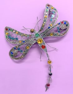 Metal and multi-colored beaded dragonfly hanging on a lilac-colored wall in Dr Shelley's office.